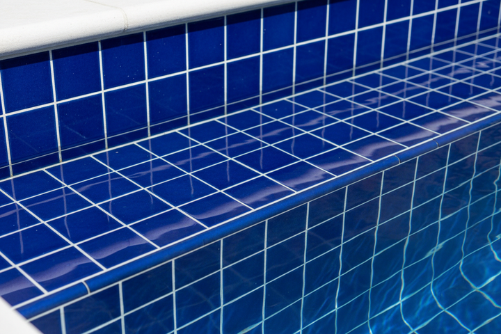 Cobalt blue 2x2 glossy pool tiles installed at waterline with crystal clear water